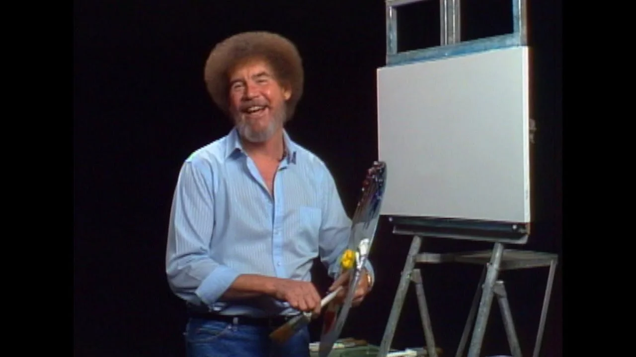 Bob Ross smiles in front of a blank canvas.