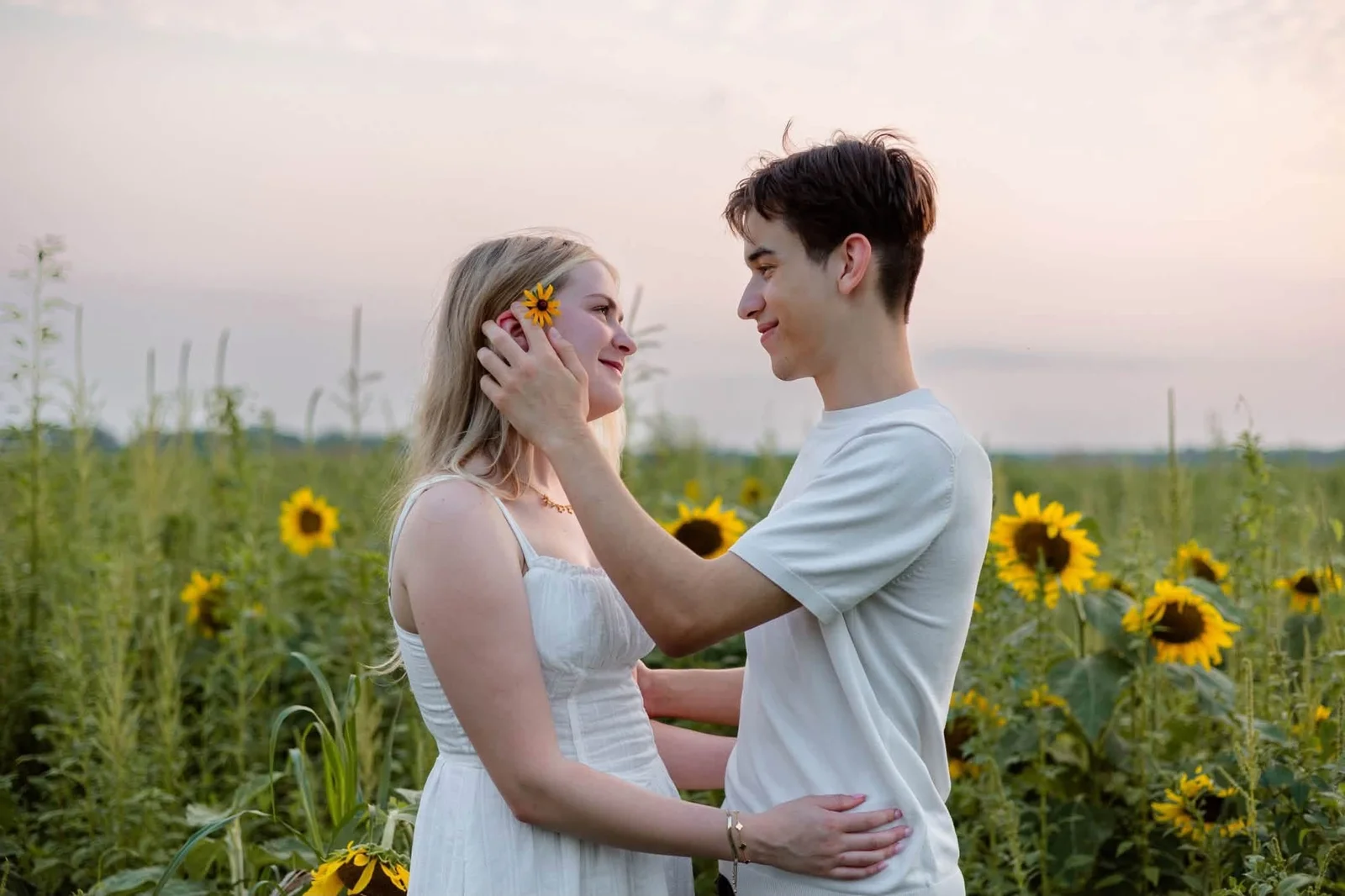Johnny and Savannah embracing in a sunflower field at sunset, Savannah wearing a white dress with a yellow flower in her hair.