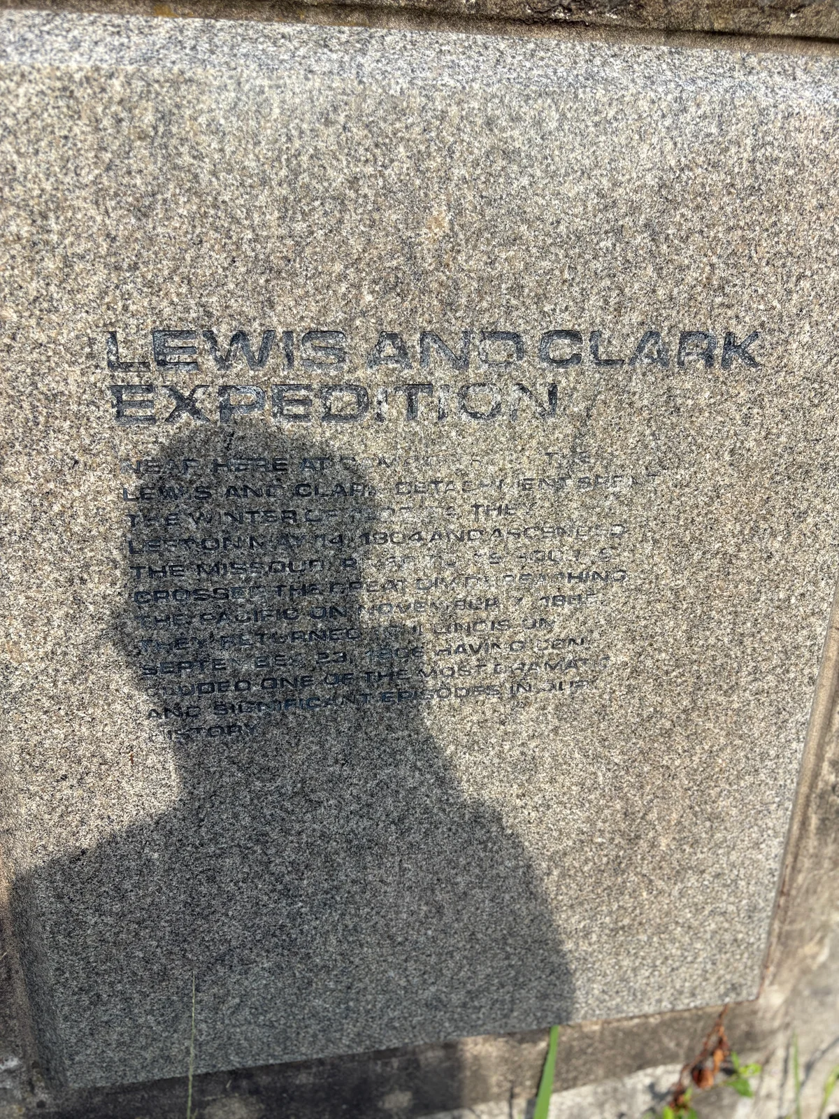 Close-up of the weathered Lewis and Clark Expedition inscription carved in granite, with my shadow, cap and all, falling across the faded text.