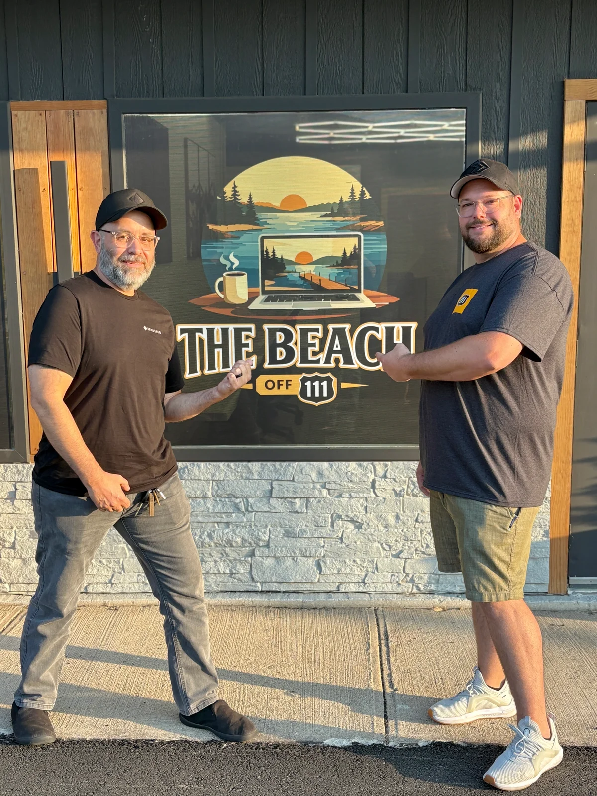 Mike and I stand in front of "The Beach Off 111" storefront sign, which features a laptop displaying a sunset landscape with a coffee mug.