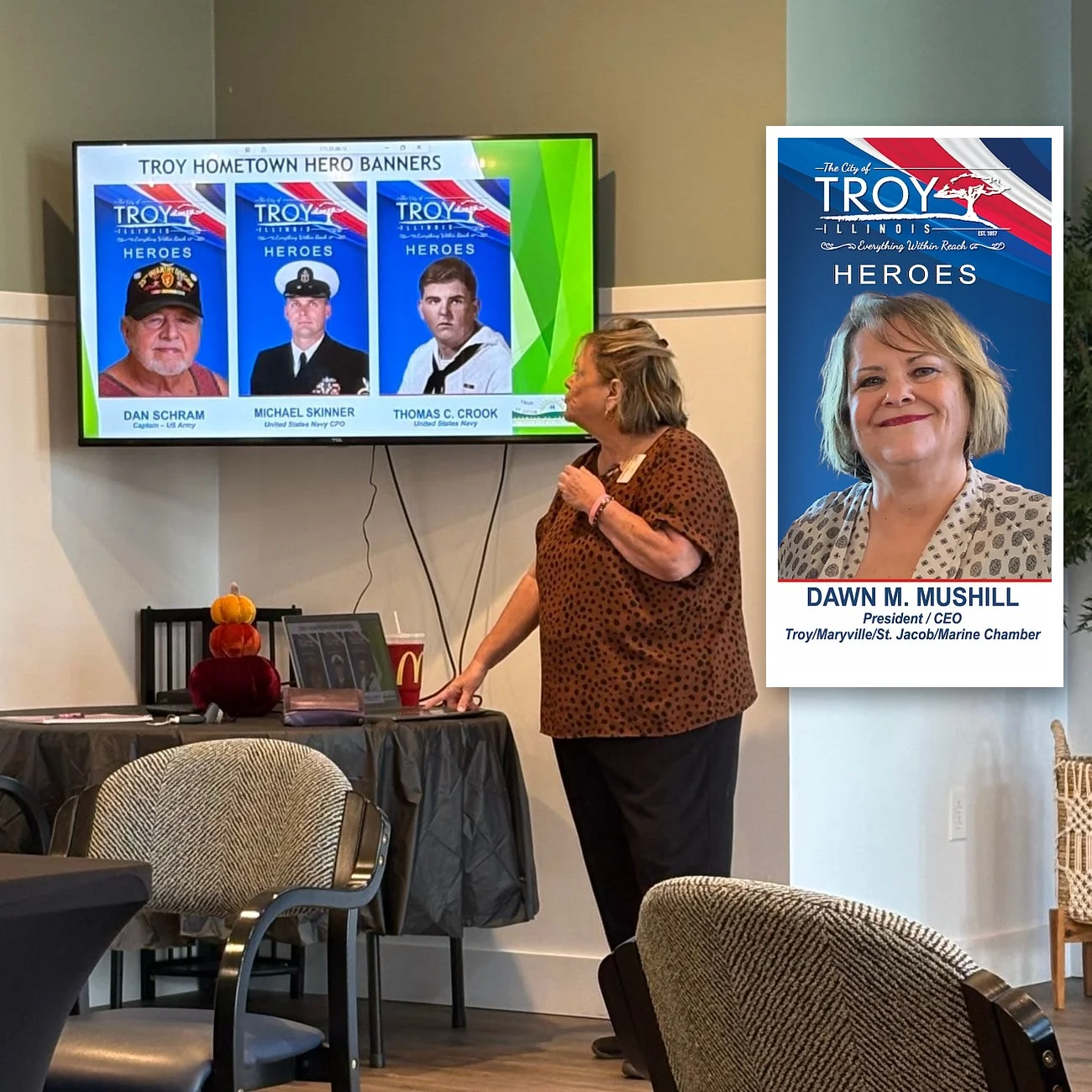 Dawn Mushill looks up at a slide titled Troy Hometown Hero Banners, showing three banner portraits of local servicemen; her own Hometown Heroes banner, with her portrait and her title, President/CEO of the Troy/Maryville/St. Jacob/Marine Chamber, is laid alongside the screen as an inset.